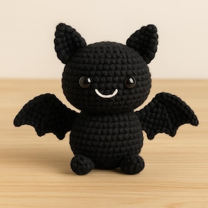 Puede incluir: Un murciélago negro de ganchillo hecho a mano con ojos grandes y redondos y una boca sonriente. El murciélago tiene orejas puntiagudas y alas extendidas. Este peluche es una linda y tierna decoración de Halloween.