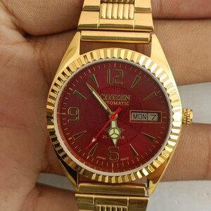 May include: Gold-coloured Citizen automatic watch with a red dial. The watch has a day-date display and a gold-coloured bracelet. The dial displays the Citizen logo and the day of the week.