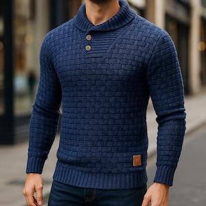 May include: A navy blue knitted sweater with a textured, brick-like pattern. The sweater has a shawl collar with two brown buttons and ribbed cuffs and hem. A small, brown leather patch is sewn on the lower right side.
