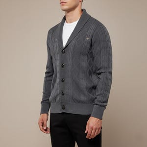 K&ouml;nnte beinhalten: Dunkelgraue Strickjacke mit Schalkragen und Knopfverschluss. Der Strickpullover hat ein Rauten- und Rippenmuster. Das Model tr&auml;gt ein wei&szlig;es T-Shirt und eine schwarze Hose.