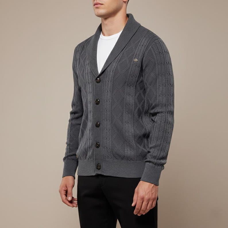 K&ouml;nnte beinhalten: Dunkelgraue Strickjacke mit Schalkragen und Knopfverschluss. Der Strickpullover hat ein Rauten- und Rippenmuster. Das Model tr&auml;gt ein wei&szlig;es T-Shirt und eine schwarze Hose.