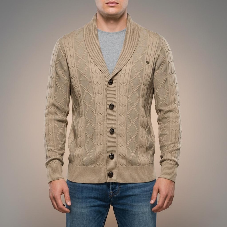K&ouml;nnte beinhalten: Beigefarbene Strickjacke mit Schalkragen und Knopfleiste. Der Cardigan hat ein Rautenmuster und gerippte B&uuml;ndchen. Die Person tr&auml;gt ein graues T-Shirt und blaue Jeans.