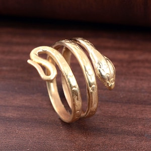 Peut inclure: Une bague dorée en forme de serpent, enroulée sur elle-même. La tête du serpent est détaillée avec des écailles et des yeux. La bague est faite d'un matériau métallique brillant.