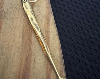 Op de afbeelding: Een goudkleurige vishangerketting. De hanger is een gestileerde vis met een gedetailleerd oog en staartvin, hangend aan een fijne zilveren ketting. De ketting wordt gepresenteerd op een houten oppervlak.