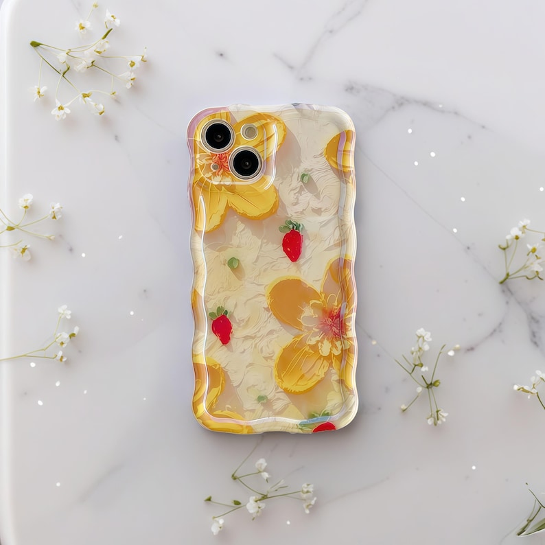 May include: Clear phone case with a yellow floral design and small red strawberry accents. The case has a wavy, textured border and is set against a white marble surface with delicate white flowers.