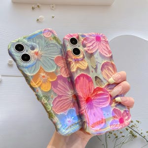 May include: Two floral phone cases. One case is a mix of blue, yellow, and green, while the other is pink and yellow. The cases have a 3D floral design. The cases are held together.