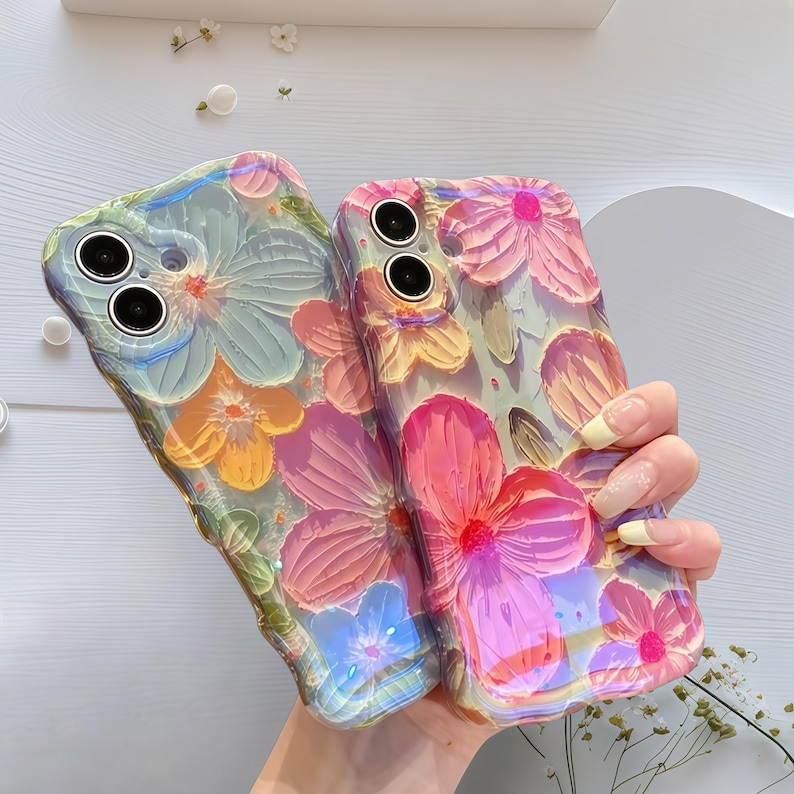 May include: Two floral phone cases. One case is a mix of blue, yellow, and green, while the other is pink and yellow. The cases have a 3D floral design. The cases are held together.