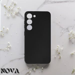 Peut inclure: Coque de téléphone noire avec trois découpes circulaires pour l'appareil photo et une seule découpe en point. Le boîtier est uni et lisse, avec le mot "NOVA" et "SHELL DESIGN" imprimés. Des fleurs blanches sont dispersées.
