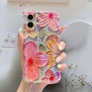 May include: A clear phone case with a 3D floral design. The flowers are in shades of pink, orange, and red, with a textured, painted appearance. The case has a glossy finish and is held in a hand.