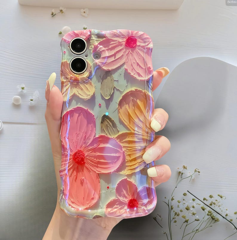 May include: A clear phone case with a 3D floral design. The flowers are in shades of pink, orange, and red, with a textured, painted appearance. The case has a glossy finish and is held in a hand.