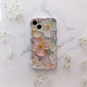 Pode incluir: Capa de telefone transparente com um design floral. A capa apresenta uma borda texturizada e ondulada e &eacute; adornada com flores brancas e rosa com centros amarelos e folhas verdes. A capa est&aacute; sobre uma superf&iacute;cie de m&aacute;rmore branco com pequenas flores brancas.