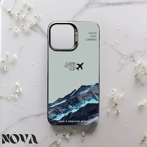 May include: A phone case with a mountain landscape design. The case features the text "CLIMB TO THE TOP" with an airplane graphic, and "NEVER STOP CLIMBING". The bottom of the case reads "KEEP A POSITIVE SPIRIT". The case has a silver camera ring and the brand name "NOVA".