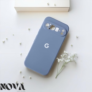 May include: A periwinkle blue phone case with a camera cutout and a white "G" logo. The case is lying on a white surface with small white flowers and a beige box. The text "NOVA SHELL DESIGN" is at the bottom.
