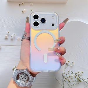Peut inclure: Coque de téléphone transparente avec un dégradé de jaune, d'orange et de violet. L'étui présente un motif circulaire blanc et un motif rectangulaire blanc. L'étui est tenu par une main avec de longs ongles décorés et une bague argentée.