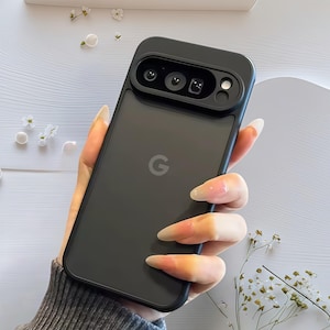 Può includere: Una custodia per telefono nera con protezione per l'obiettivo della fotocamera. La custodia ha una finitura opaca e presenta il logo "G" di Google. La protezione dell'obiettivo della fotocamera ha tre aperture circolari per gli obiettivi.