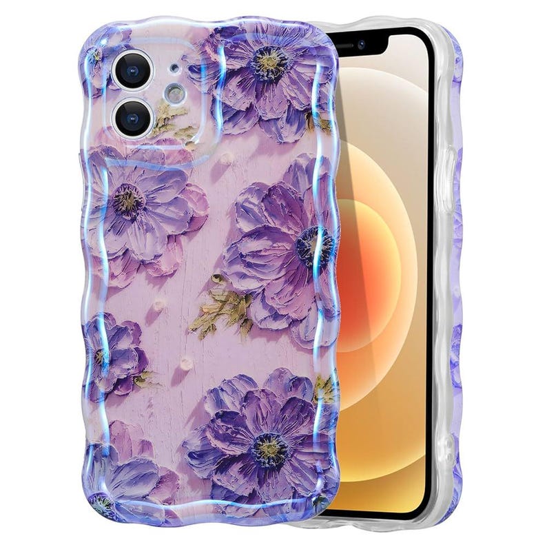 Pode incluir: Uma capa de telefone transparente com um design floral. A capa apresenta grandes flores roxas com detalhes verdes em um fundo rosa claro. A capa tem uma borda ondulada e texturizada e &eacute; mostrada em um smartphone.