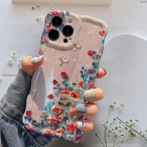 Pode incluir: Capa de telem&oacute;vel floral com fundo rosa e borda ondulada. O design apresenta flores vermelhas, azuis e brancas. A capa tem um acabamento transparente e brilhante.