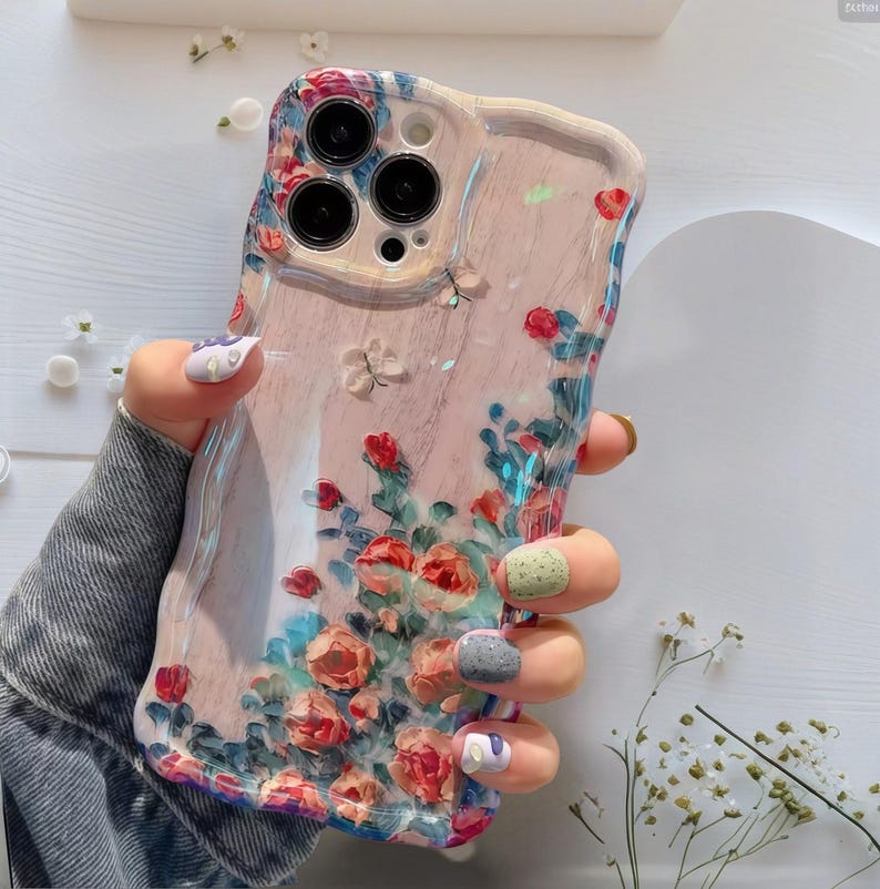 Pode incluir: Capa de telem&oacute;vel floral com fundo rosa e borda ondulada. O design apresenta flores vermelhas, azuis e brancas. A capa tem um acabamento transparente e brilhante.