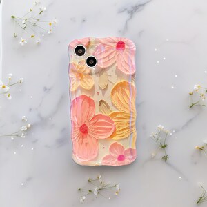 May include: A clear phone case featuring a floral design with pink, peach, and yellow flowers. The case has a textured, raised surface, and the flowers have a painted appearance. The case has cutouts for the phone's camera.