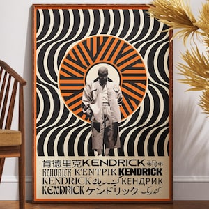 以下が含まれることがあります： オレンジと黒の同心円と波線模様を背景に、コートを着た人物の白黒写真が描かれた額入りのポスター。ポスターには、複数の言語で「KENDRICK」という名前が記載されています。木製の椅子と装飾用の植物が前景にあります。