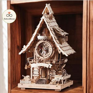 May include: A wooden clock model with a whimsical house design. The clock features a detailed facade with a clock face, a small balcony, and the word "Wonderland" at the base. The clock is made of light-colored wood and sits on a wooden shelf.