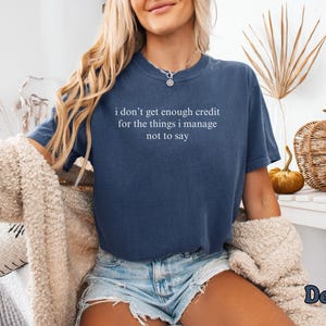 K&ouml;nnte beinhalten: Marineblaues T-Shirt mit dem wei&szlig;en Text "i don't get enough credit for the things i manage not to say". Das Shirt wird mit Jeansshorts kombiniert. Das Wort "Denim" ist unten rechts sichtbar.
