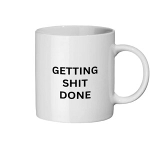 Könnte beinhalten: Weißer Keramikbecher mit schwarzem Henkel. Der Becher trägt den Schriftzug "GETTING SHIT DONE" in fetten, schwarzen Großbuchstaben. Der Becher ist zylindrisch und hat ein schlichtes, klares Design, geeignet für Kaffee oder Tee.