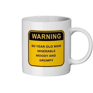 May include: White ceramic mug with a black and yellow warning label. The label reads "WARNING" at the top, followed by "60 YEAR OLD MAN MISERABLE MOODY AND GRUMPY" in black text.