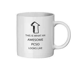 May include: A white ceramic mug featuring a black arrow graphic and the text "THIS IS WHAT AN AWESOME PCSO LOOKS LIKE". The mug has a curved handle and is designed for hot drinks.