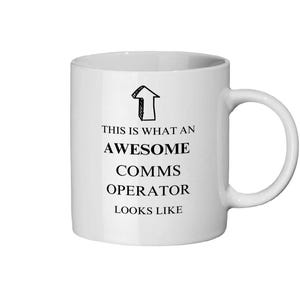 May include: White ceramic mug with a black arrow graphic and the text "THIS IS WHAT AN AWESOME COMMS OPERATOR LOOKS LIKE". The mug has a curved handle and is suitable for hot or cold drinks.