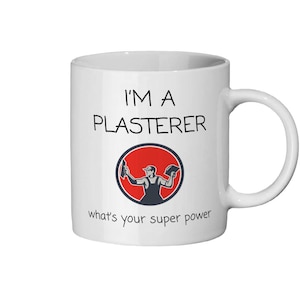 以下が含まれることがあります： 「I'M A PLASTERER」の黒い文字が入った白いセラミックマグ。その下に、赤い円の中に左官屋の円形グラフィックがあります。「what's your super power」というテキストがグラフィックの下にあります。