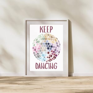 Puede incluir: Impresión enmarcada con una ilustración de bola de discoteca colorida. Las palabras "KEEP DANCING" están escritas en borgoña arriba y abajo de la bola de discoteca. La impresión se muestra en un marco blanco.