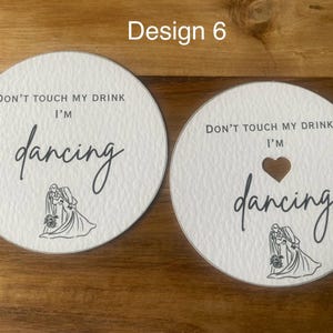 May include: Two white round coasters with the text "DON'T TOUCH MY DRINK I'M dancing" in black script. One coaster has a heart-shaped cutout. Both have a line drawing of a couple dancing.