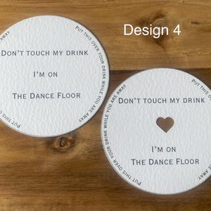 May include: Two white drink coasters with the text "Don't touch my drink, I'm on the dance floor." One coaster has a heart-shaped cutout. The phrase "Put this over your drink while you are away" is printed around the edge.