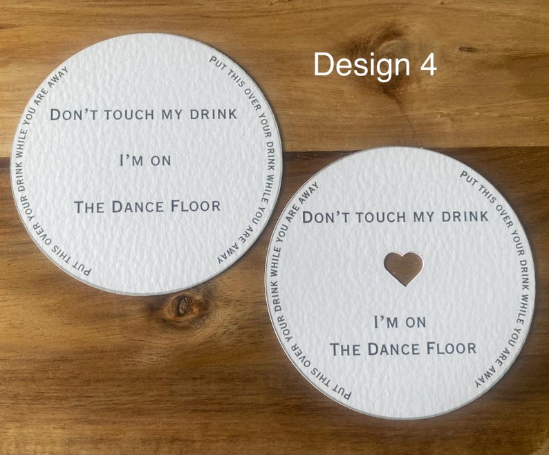May include: Two white drink coasters with the text "Don't touch my drink, I'm on the dance floor." One coaster has a heart-shaped cutout. The phrase "Put this over your drink while you are away" is printed around the edge.
