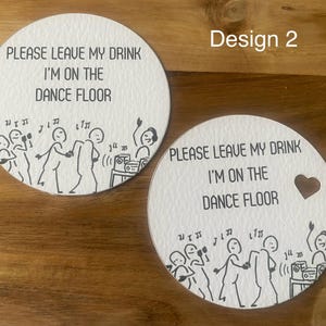 May include: Two white, round coasters with a black illustration of dancing figures and the text "PLEASE LEAVE MY DRINK I'M ON THE DANCE FLOOR." One coaster has a heart-shaped cutout. The design includes musical notes and a stereo.