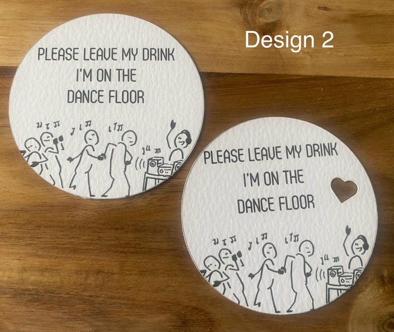 May include: Two white, round coasters with a black illustration of dancing figures and the text "PLEASE LEAVE MY DRINK I'M ON THE DANCE FLOOR." One coaster has a heart-shaped cutout. The design includes musical notes and a stereo.