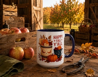 May include: A white ceramic mug with a dark blue interior and handle, featuring a colorful illustration of apples, oranges, berries, and a pumpkin. The text "HAPPY FALL Y'ALL" is printed in red letters on the front of the mug.
