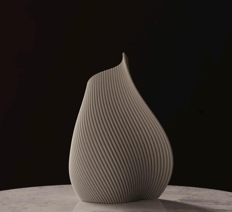 May include: A light gray, modern vase with a unique, curved design. The vase has a textured surface with vertical lines that spiral around the body. The vase is set against a dark background.