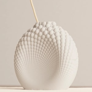 May include: A white, textured ceramic vase with a unique, bubble-like pattern. The vase has a rounded shape and a small opening at the top, with a thin, light-colored stem extending from it. The design creates a visually interesting and modern aesthetic.