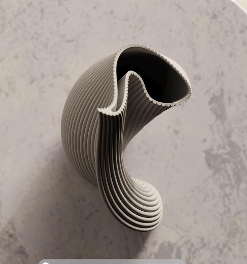 May include: A modern, abstract vase in shades of gray. The vase has a unique, curved shape with vertical ridges and a scalloped edge. The interior is dark, creating a contrast with the light exterior. The design is minimalist and sculptural.