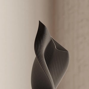 May include: A gray, abstract sculpture with a spiraling, ribbed design. The form curves upwards, creating a dynamic and modern aesthetic. The sculpture's surface has a textured appearance, and the background is a neutral beige.