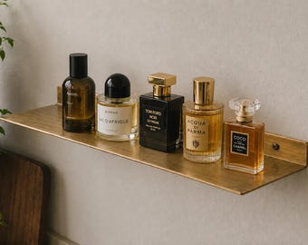 May include: A rectangular brass wall shelf with a brushed finish holds five glass perfume bottles. The bottles feature various shapes and labels including Aesop, Byredo Bal d'Afrique, Tom Ford Noir Extreme, Acqua di Parma, and Chanel Coco Eau de Parfum.