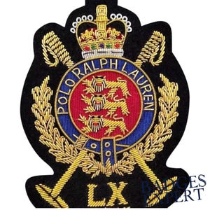 Peut inclure: Écusson brodé sur fond noir, orné d'une couronne dorée, de feuilles de laurier et des mots "POLO RALPH LAUREN" dans un cercle bleu. Le centre présente trois lions dorés sur fond rouge. Épées croisées dorées et lettres "LX" en bas.