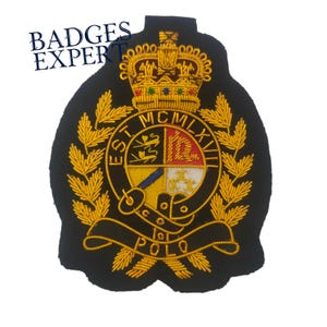 Pode incluir: Patch bordado preto com coroa dourada, folhas de louro e um emblema central com um design de escudo. O patch inclui o texto "EST MCMXVII" e "POLO". As palavras "BADGES EXPERT" estão no canto superior esquerdo.