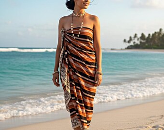 May include: A woman stands on a sandy beach wearing a striped sarong. The sarong features alternating bands of black, brown, and orange. She wears a shell necklace and bracelets. The background includes the ocean, blue sky, and a tropical island.