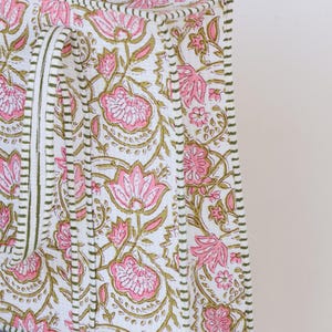 May include: A white tote bag with a pink floral pattern and olive green accents. The bag features a repeating design of stylized flowers and leaves. The edges are trimmed with a green stitched border.
