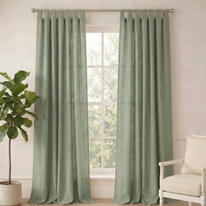 以下が含まれることがあります： 窓を囲むように、シルバーのロッドに吊るされたセージグリーンのリネンカーテン。鉢植えの植物と、クリーム色のクッションが付いた白い椅子が両側にあります。天然繊維のラグが床を覆っています。