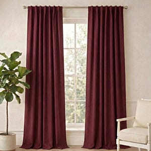 Peut inclure: Rideaux bordeaux, longs jusqu'au sol, suspendus à une tringle argentée, encadrent une fenêtre. Un pot de plante et une chaise blanche avec un coussin crème sont de chaque côté de la fenêtre. Un tapis tissé recouvre le sol.