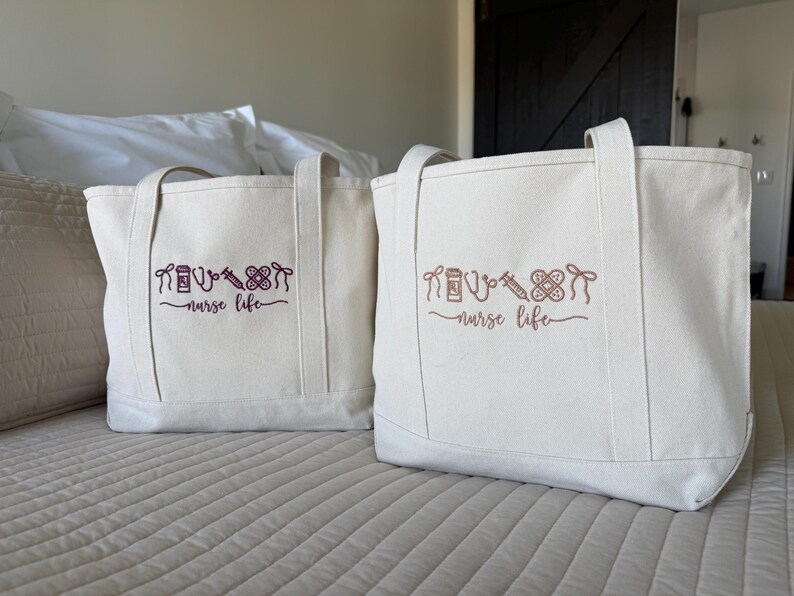 May include: Two off-white canvas tote bags with matching handles. Each bag features a design of medical symbols and the words "nurse life" in a cursive font. The bags are sitting on a bed.